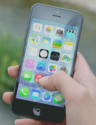Picture of a hand holding a mobile phone displaying its home page full of various apps.