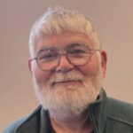 Graham Pope. A smiling man with grey hair and beard, wearing large, rounded glasses.